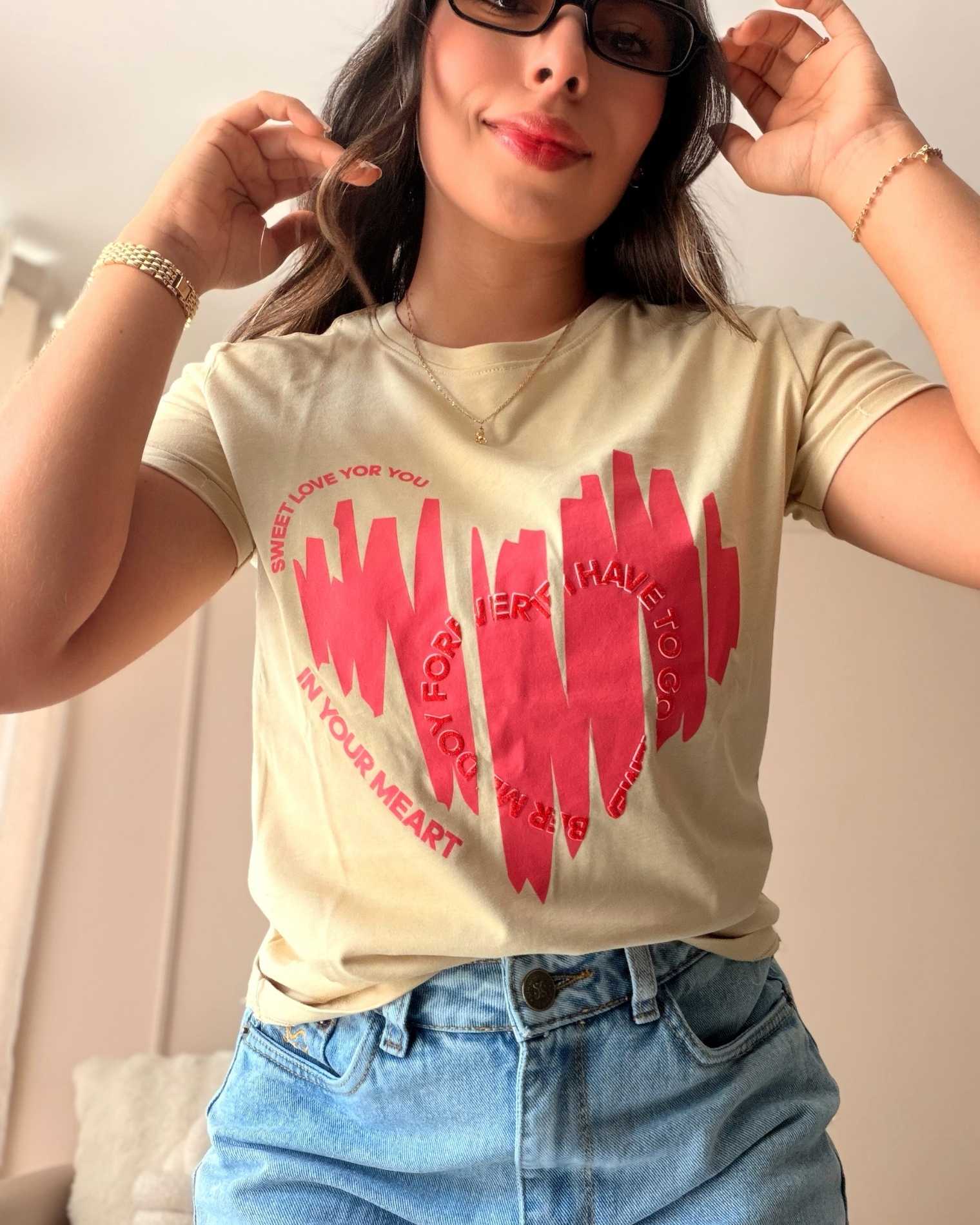 Modelo luciendo camiseta beige de mujer con tierno diseño de corazón rosa, estilo casual y cómodo, calidad premium en algodón de la marca Mozzaar.