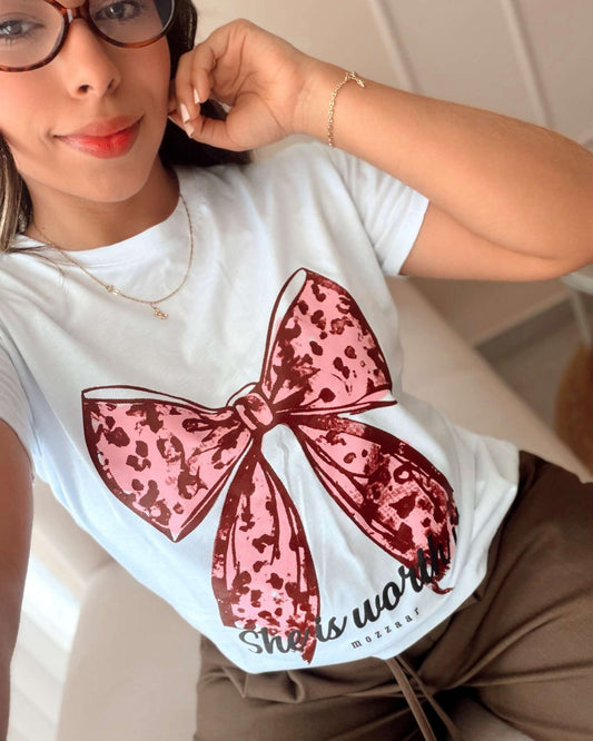 Camiseta blanca de mujer con diseño de moño en animal print rosa y la frase "She is worth", marca Mozzaar, silueta femenina en algodón premium.