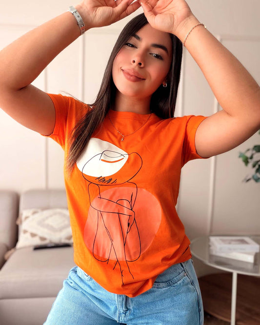 Camiseta naranja para mujer con ilustración lineal de mujer con sombrero, marca Mozzaar, confeccionada en 100% algodón Pima.
